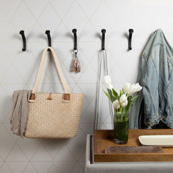 Six Black Cast Iron Railway Spike Wall Mount Hooks in an entryway holding a purse, keys, a jacket, and a belt.