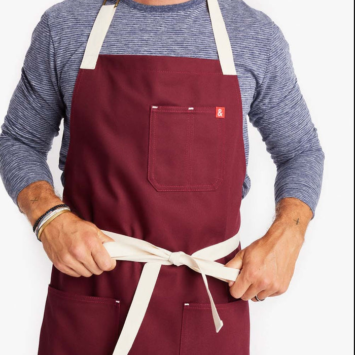 Man tying marshmallow-hued straps on Bordeaux Crossback Apron