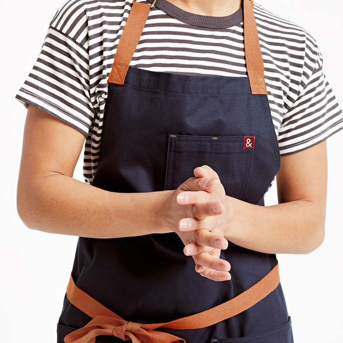Woman wearing midnight blue apron with her hands clasped