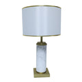 White marble cylinder table lamp with brass metal base and brass trim fabric shade turned off on white background