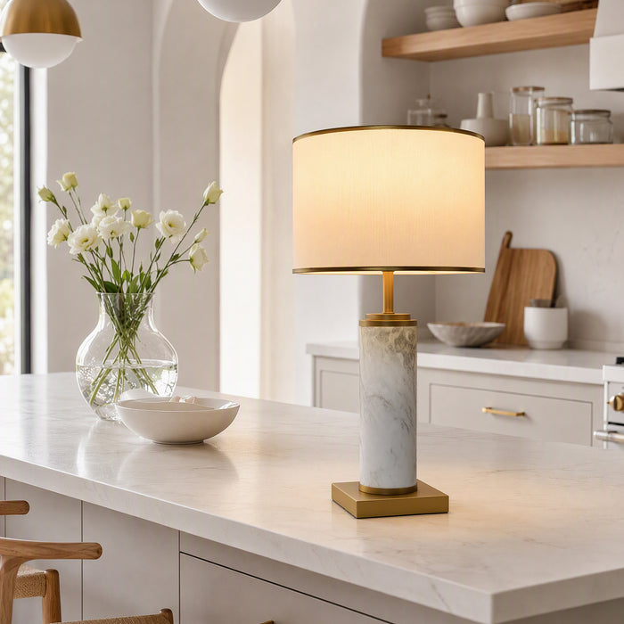Illuminated white marble table lamp on marble kitchen island counter beside vase with flowers