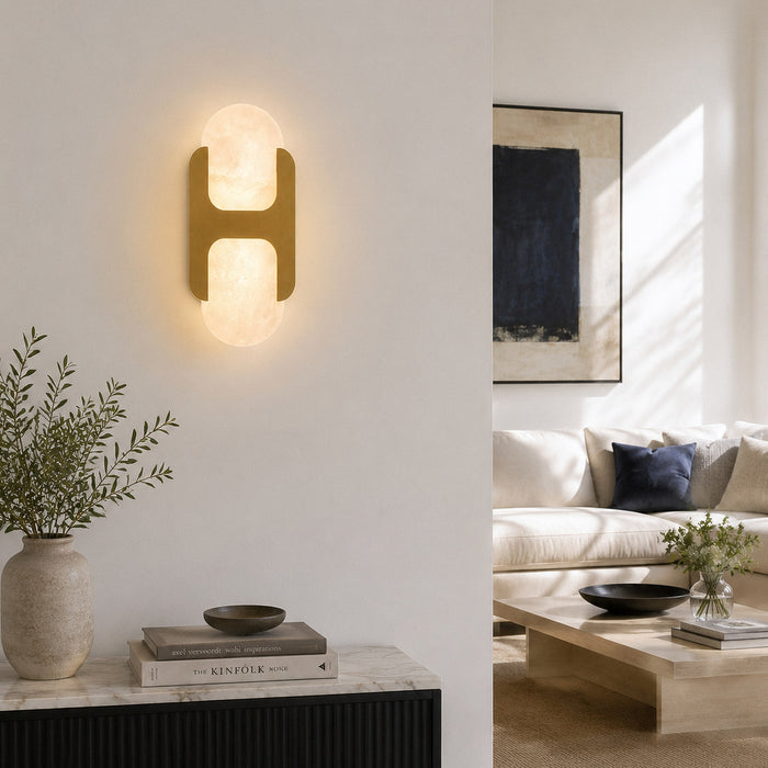 Illuminated brass and Spanish alabaster wall sconce mounted above a console table in a modern living room entryway corner