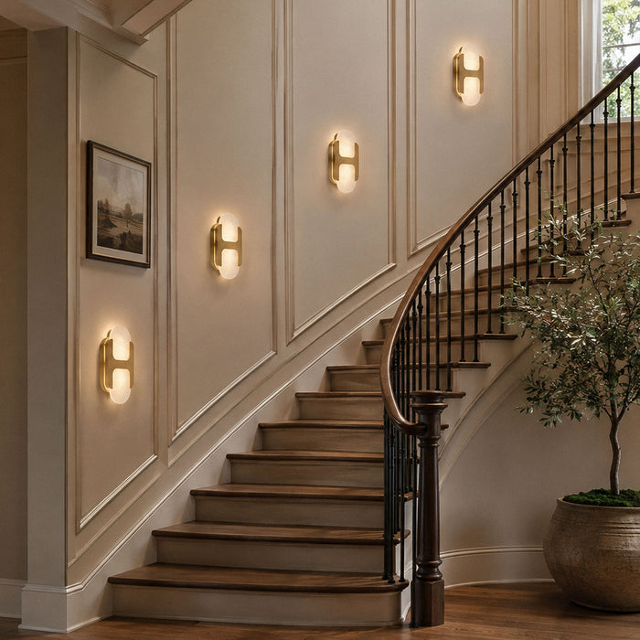 Multiple illuminated brass alabaster wall sconces mounted on a grand curved staircase wall creating warm lighting ambiance