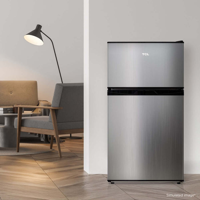 TCL 18 in. 3.1 Cu. Ft. Compact Top Freezer Mini Fridge in Silver (TRM31D4AV) in a modern living room setting with a lamp and sofa.