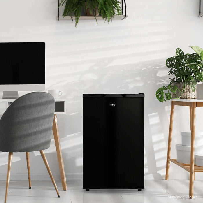 TCL 21 in. 4.5 Cu. Ft. Compact Single Door Mini Fridge in Black (TRM45S4AB) in a modern room with a chair, table, and plants.