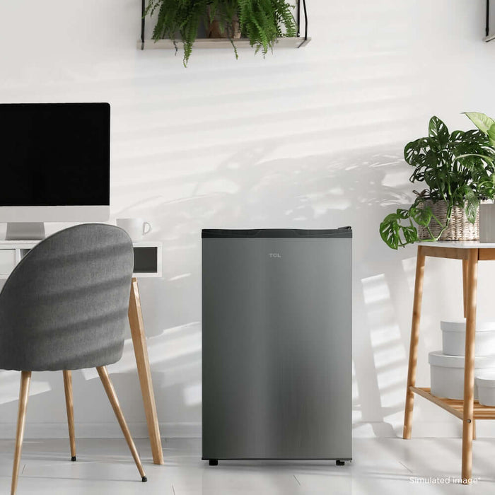 TCL 21 in. 4.5 Cu. Ft. Compact Single Door Mini Fridge in Silver (TRM45S4AV) in a modern room with a chair, table, and plants.