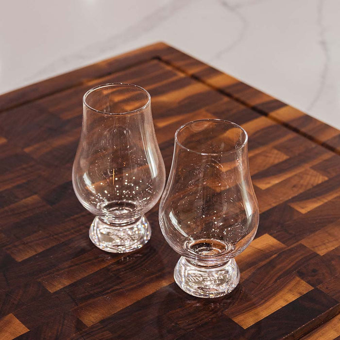 Two empty whiskey glasses on wooden cutting board.