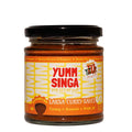 A jar of Yumm Singa Laksa Curry Sauce with a bright orange label and red branding on a white background